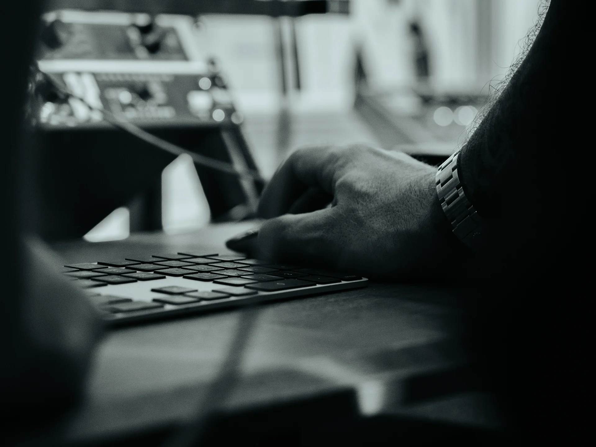 Hands at the desk keyboard in the control room, the outboard rack behind in shallow focus.